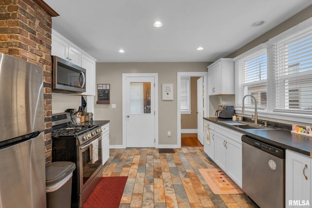 kitchen with dark countertops, a sink, baseboards, appliances with stainless steel finishes, and white cabinetry