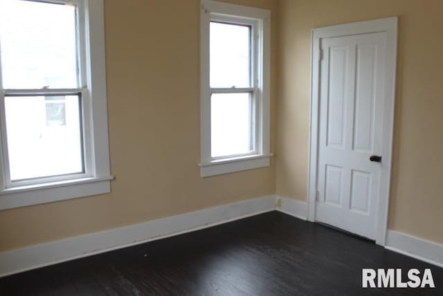 empty room featuring baseboards, a wealth of natural light, and dark wood-style floors