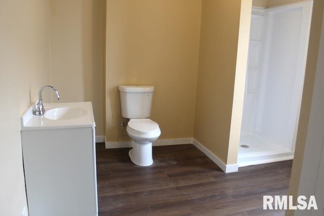 bathroom with a stall shower, toilet, baseboards, wood finished floors, and vanity