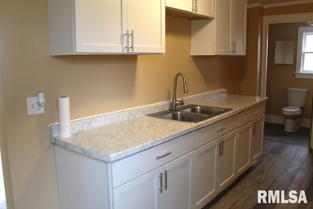kitchen with a sink, dark wood finished floors, baseboards, white cabinetry, and light stone counters