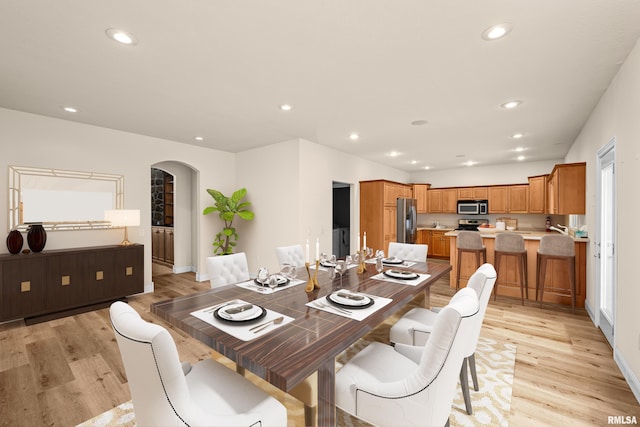 dining area with arched walkways, light wood-style floors, baseboards, and recessed lighting
