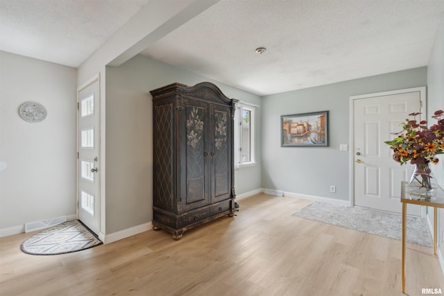 entrance foyer featuring visible vents, a textured ceiling, light wood finished floors, and baseboards