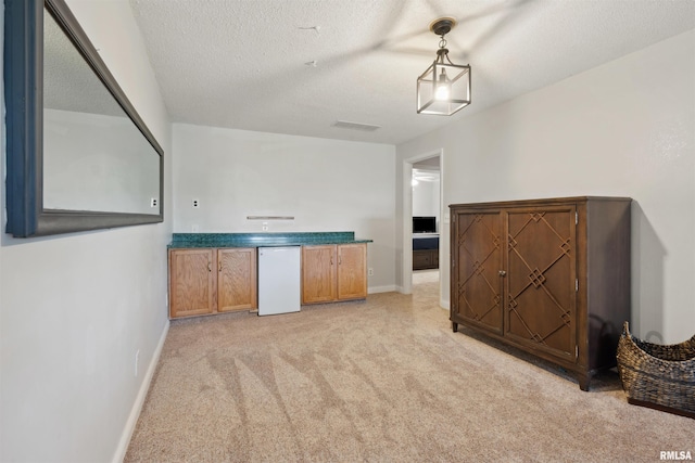 kitchen with a textured ceiling, hanging light fixtures, brown cabinets, baseboards, and light carpet