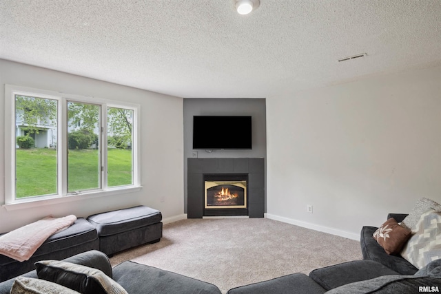 carpeted living area with baseboards, a fireplace, a textured ceiling, and visible vents