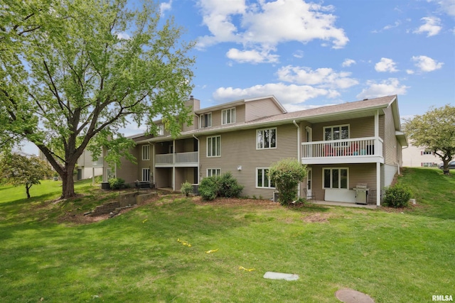 rear view of property with a yard, a patio, a chimney, and a balcony