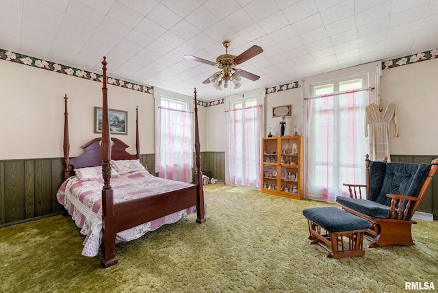 carpeted bedroom featuring wainscoting, wood walls, and ceiling fan
