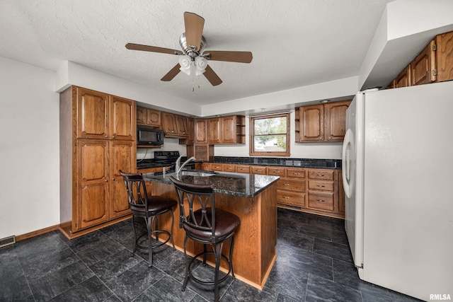kitchen featuring freestanding refrigerator, brown cabinets, and black microwave