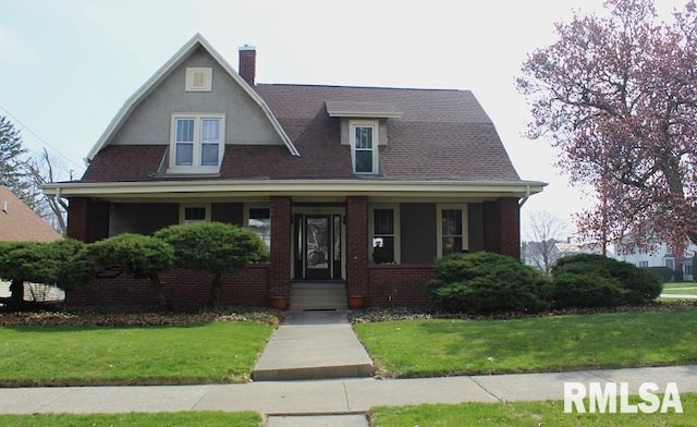 view of front facade with a chimney, a front lawn, brick siding, and a porch