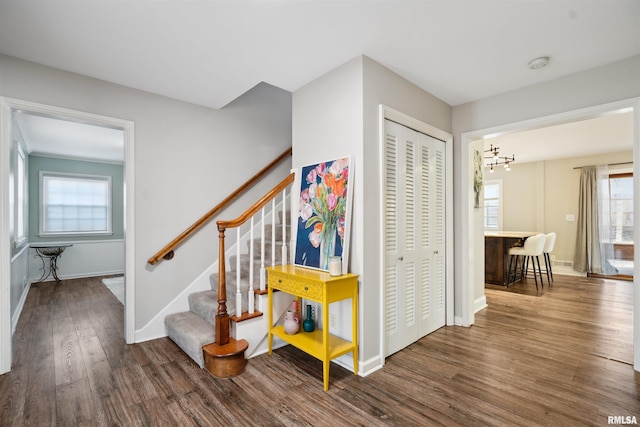 stairs featuring wood finished floors, a healthy amount of sunlight, baseboards, and an inviting chandelier