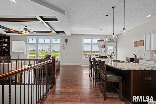 kitchen with light stone counters, ceiling fan, a sink, dark wood-style floors, and a textured ceiling