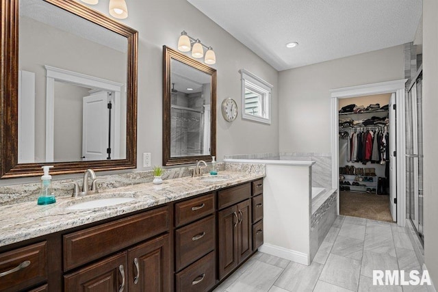 full bath with double vanity, a textured ceiling, a stall shower, and a sink