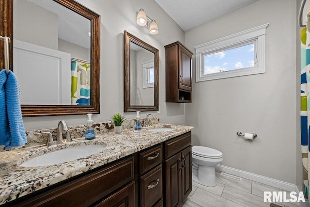 bathroom with toilet, double vanity, a sink, and baseboards