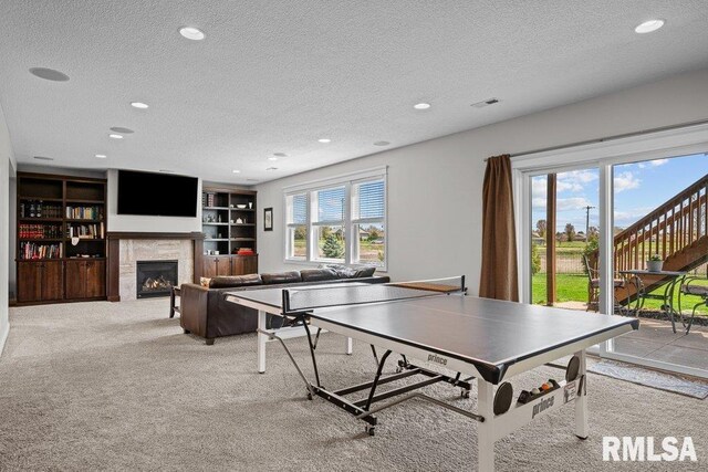 rec room featuring a textured ceiling, visible vents, a lit fireplace, and carpet