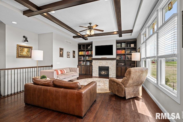 living area featuring beamed ceiling, a ceiling fan, a stone fireplace, and dark wood-type flooring