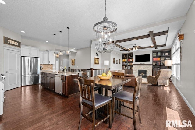 dining area with coffered ceiling, ceiling fan with notable chandelier, a fireplace, beam ceiling, and dark wood-type flooring