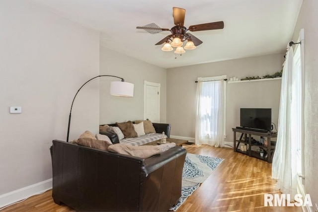 living room with light wood-style flooring, a ceiling fan, and baseboards