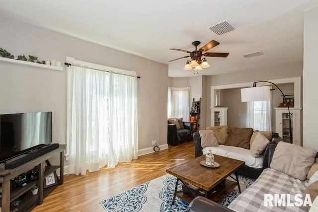 living room featuring baseboards, wood finished floors, visible vents, and ceiling fan