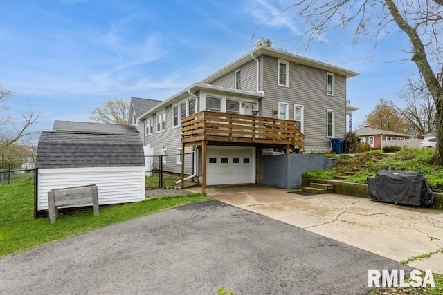 rear view of house with fence, a garage, a wooden deck, a shingled roof, and aphalt driveway