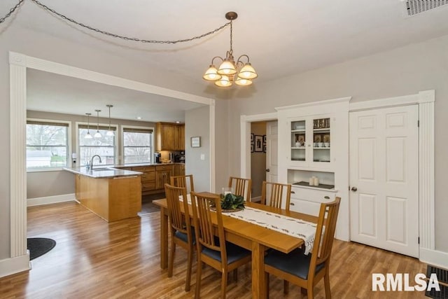 dining area featuring light wood finished floors, baseboards, visible vents, and an inviting chandelier