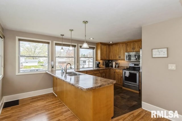 kitchen featuring a peninsula, appliances with stainless steel finishes, baseboards, and a sink