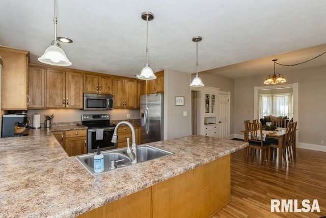 kitchen with brown cabinets, stainless steel appliances, wood finished floors, a sink, and pendant lighting