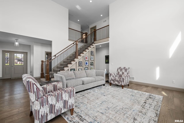 living area with visible vents, wood finished floors, baseboards, stairway, and a towering ceiling