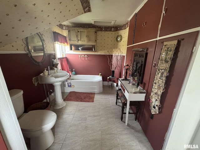bathroom with wallpapered walls, wainscoting, toilet, and a garden tub