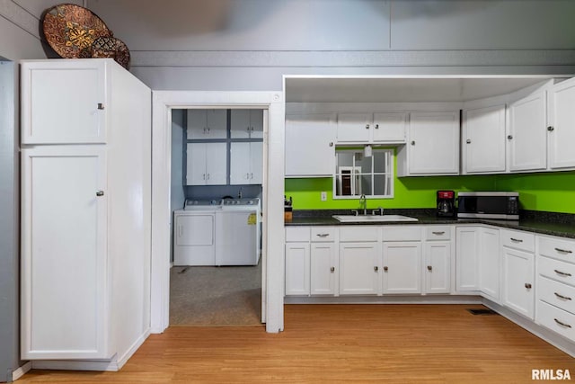 kitchen featuring stainless steel microwave, washing machine and clothes dryer, white cabinets, light wood finished floors, and a sink