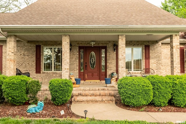 property entrance featuring brick siding, a porch, and a shingled roof
