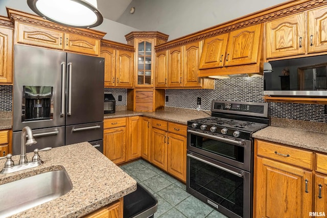 kitchen with brown cabinets, a sink, decorative backsplash, appliances with stainless steel finishes, and dark tile patterned flooring