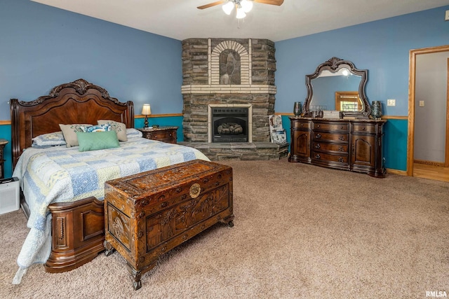 bedroom with ceiling fan, a stone fireplace, and carpet