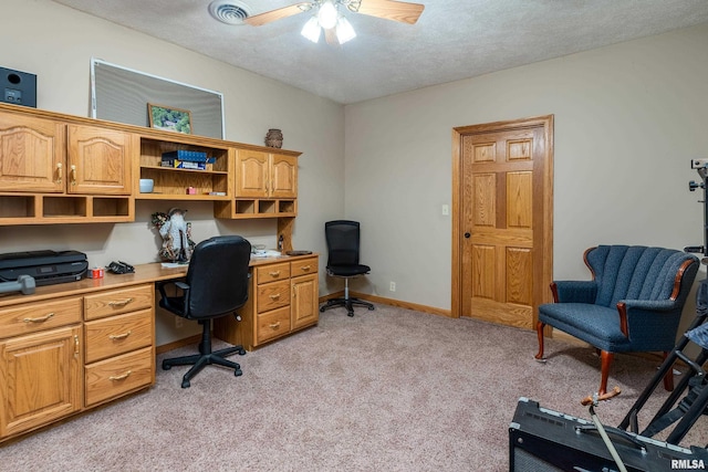 office space featuring built in desk, ceiling fan, baseboards, a textured ceiling, and light colored carpet