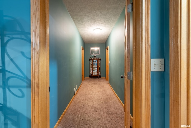 corridor featuring a textured ceiling, baseboards, and carpet floors