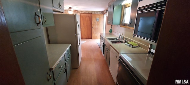 kitchen with a sink, light wood-style floors, light countertops, freestanding refrigerator, and electric range