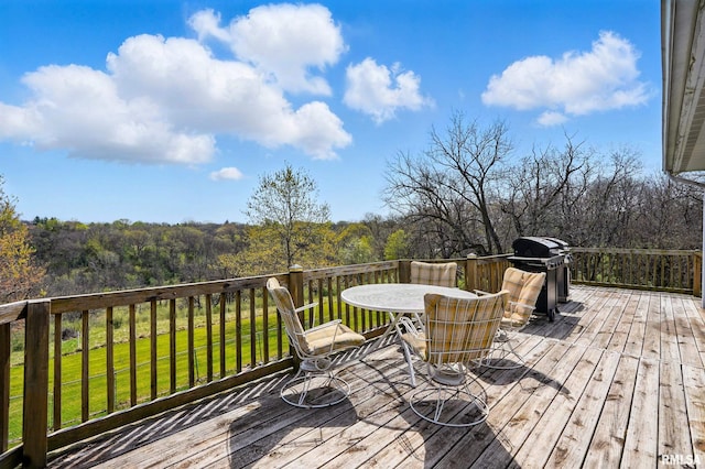 wooden terrace with a lawn, area for grilling, outdoor dining space, and a wooded view