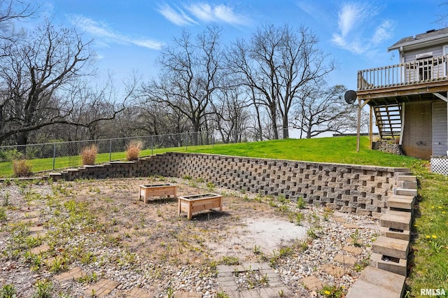 view of yard with a garden, a wooden deck, a fenced backyard, and stairs