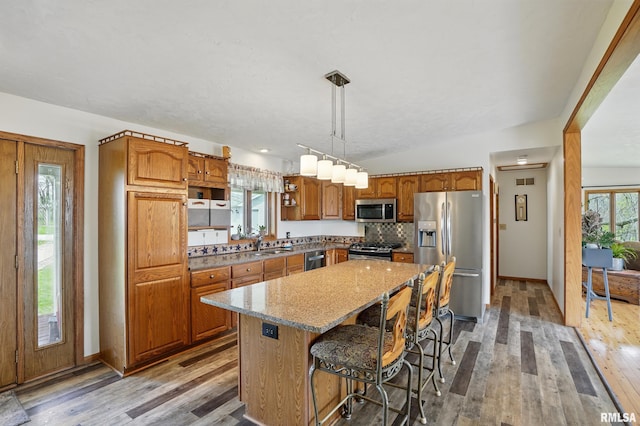 kitchen featuring brown cabinetry, open shelves, appliances with stainless steel finishes, light wood finished floors, and a center island
