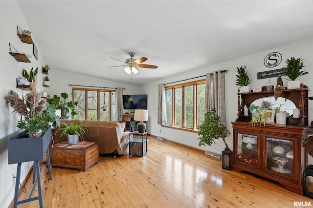 living area with hardwood / wood-style floors, visible vents, a ceiling fan, and baseboards