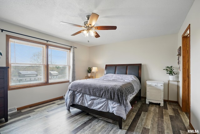 bedroom with a textured ceiling, visible vents, baseboards, wood finished floors, and a ceiling fan