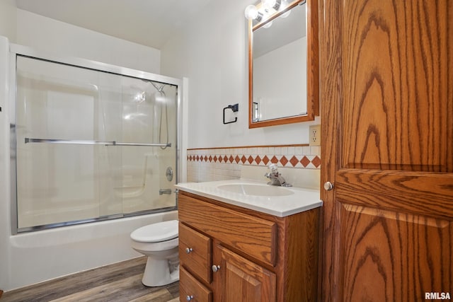 full bathroom featuring wood finished floors, wainscoting, tile walls, shower / bath combination with glass door, and vanity
