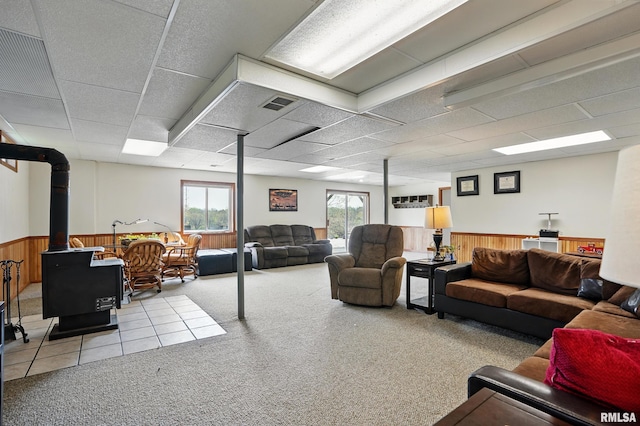 living area featuring a wainscoted wall, carpet flooring, visible vents, a wood stove, and wooden walls