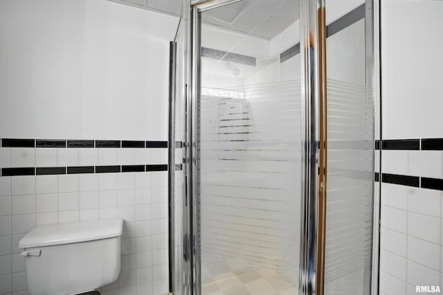 bathroom with tile walls, a shower stall, and toilet
