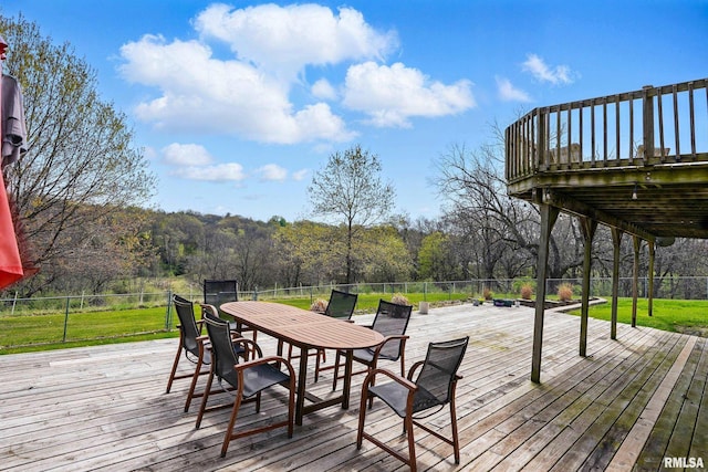wooden deck featuring a lawn, outdoor dining area, a view of trees, and fence