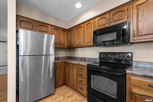 kitchen featuring brown cabinetry, black appliances, dark countertops, and light wood-style floors