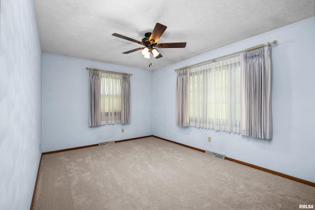 carpeted spare room with visible vents, ceiling fan, and baseboards