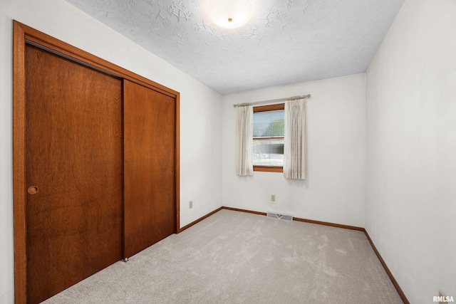 unfurnished bedroom with a textured ceiling, light colored carpet, visible vents, baseboards, and a closet