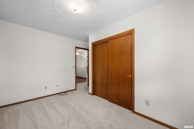 unfurnished bedroom featuring a closet, a textured ceiling, carpet floors, and baseboards