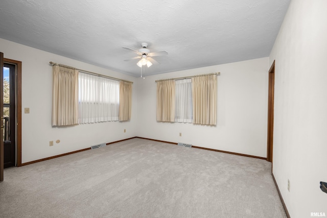 unfurnished room with a ceiling fan, visible vents, and a wealth of natural light