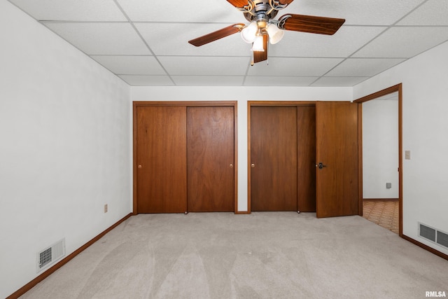 unfurnished bedroom featuring light colored carpet, visible vents, two closets, and a drop ceiling