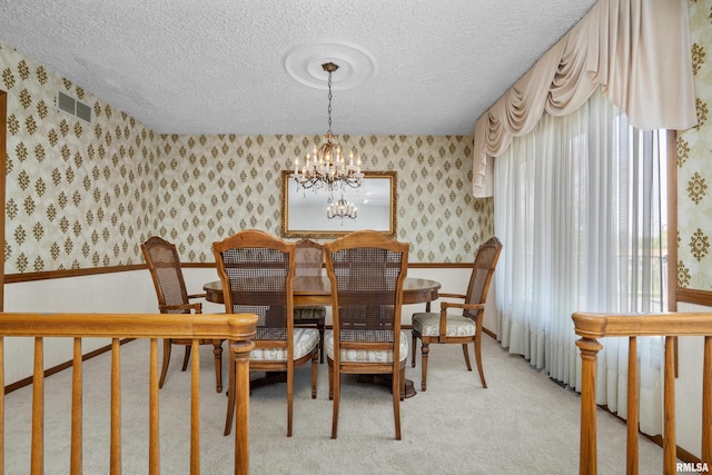 dining area with a textured ceiling, an inviting chandelier, wallpapered walls, and light colored carpet